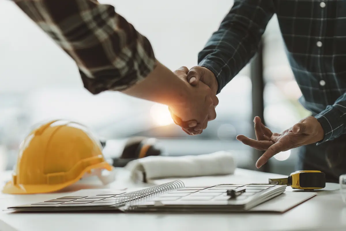 A New Horizons engineer and a client shaking hands over project drawings