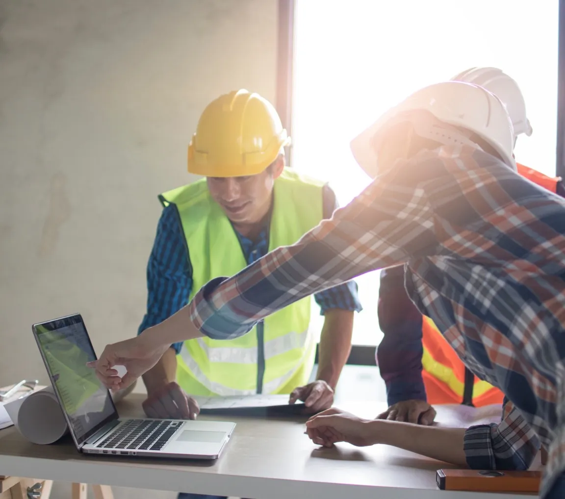 New Horizons engineers in hard hats reviewing project plans on a laptop at a construction site