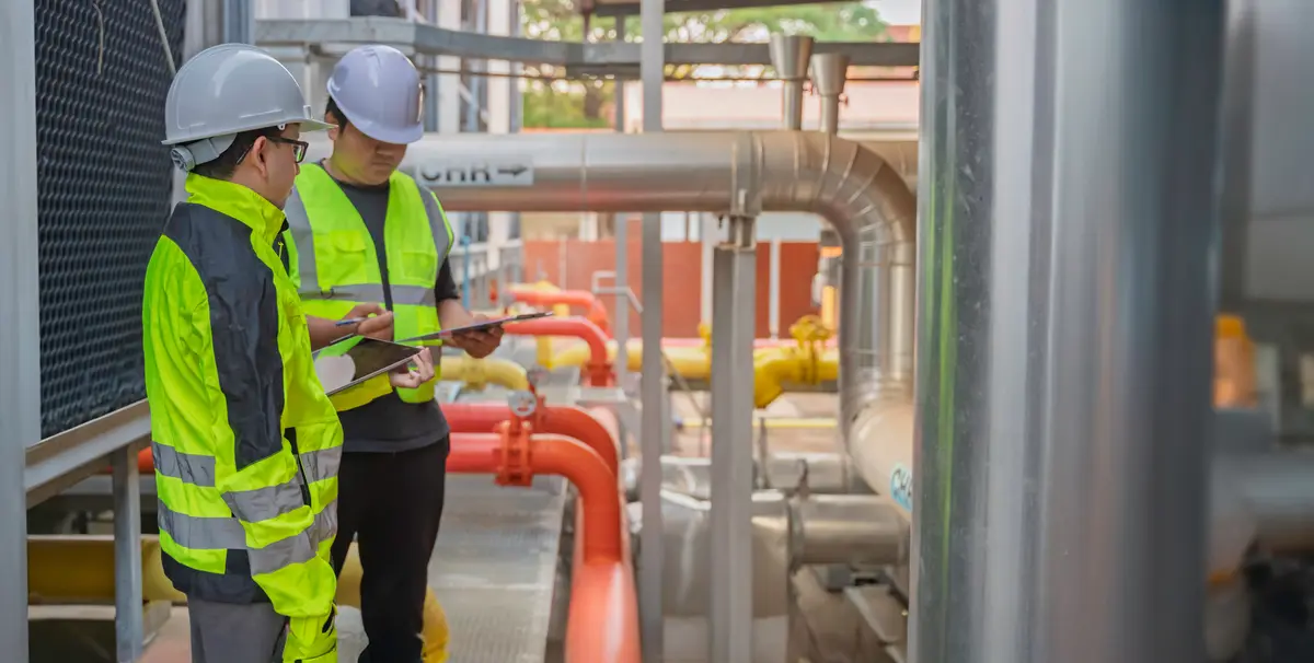 Two engineers inspecting color-coded process piping on an outdoor pipe rack